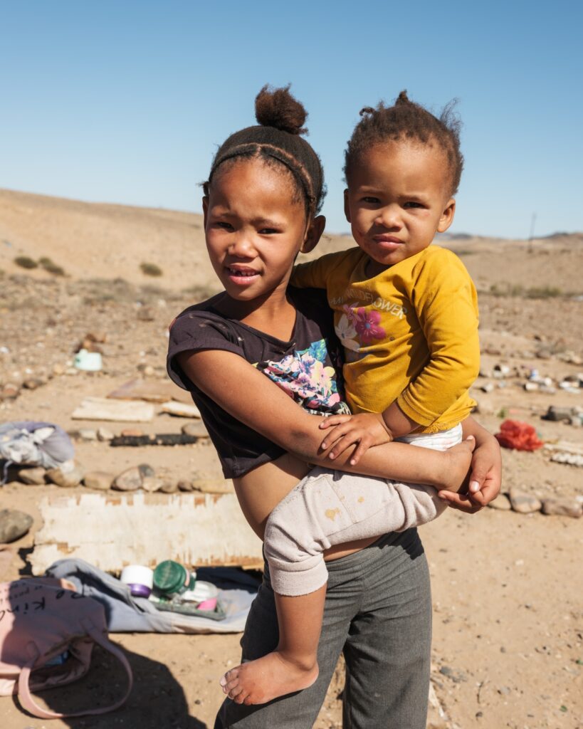 Young girl holding a small child in an arid West Coast landscape.
