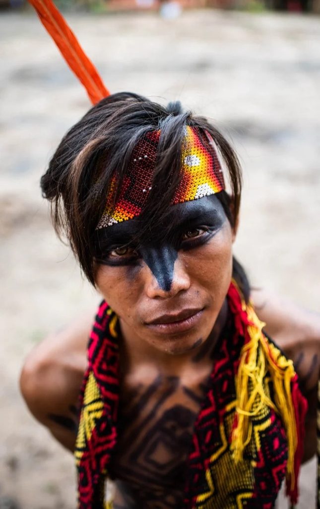 Portrait of an Indigenous man wearing traditional beadwork, a feather headpiece and black face paint.